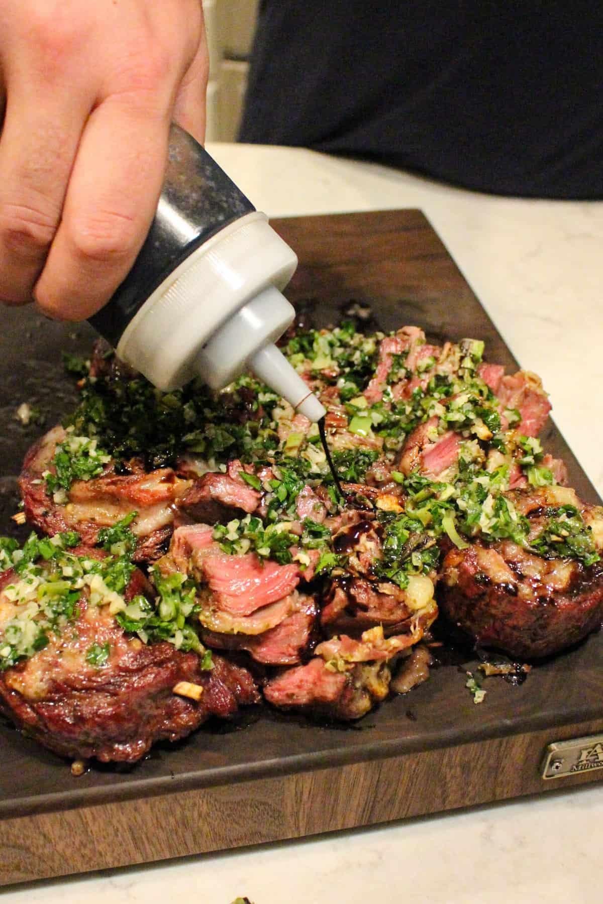balsamic vinegar being drizzled over grilled steak pinwheels with charred scallion gremolata