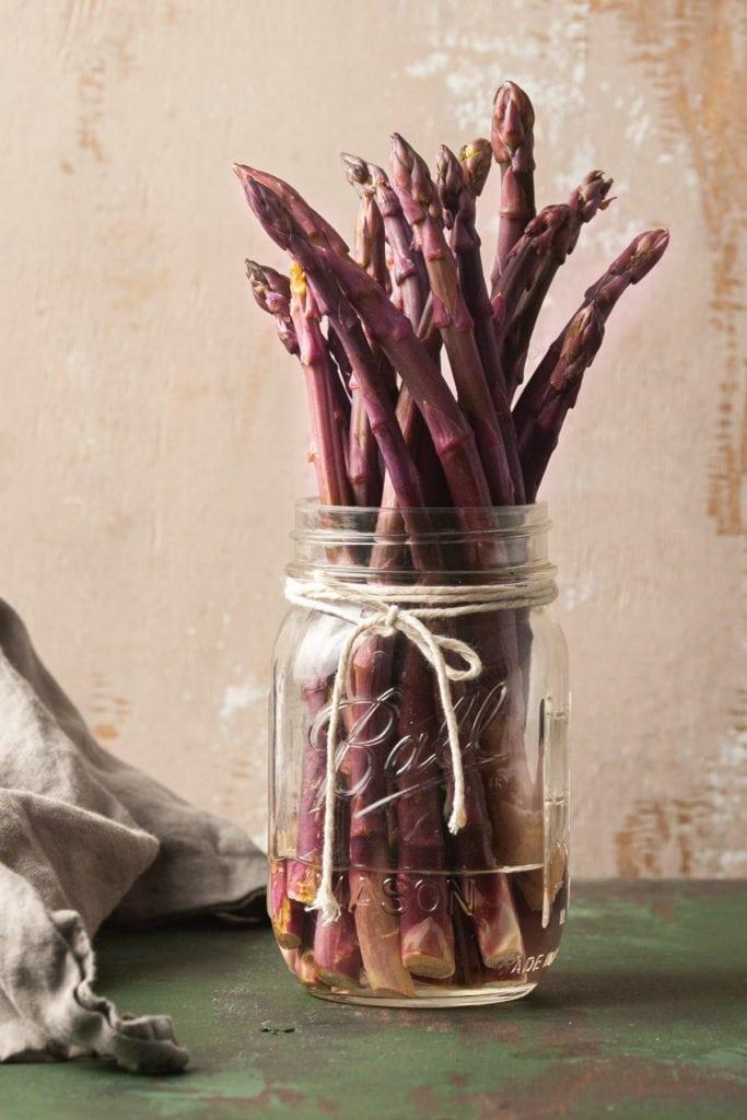 storing raw purple asparagus in a mason jar with water