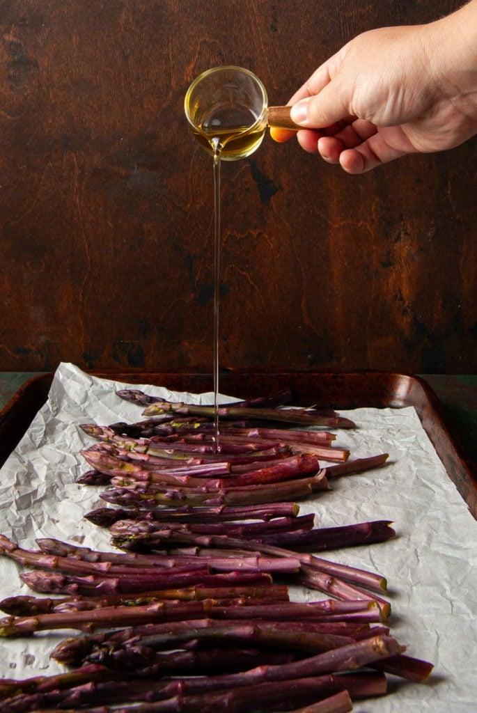 pouring olive oil on asparagus on a baking sheet