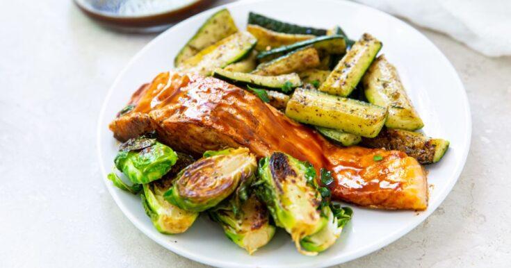 grilled teriyaki salmon with grilled zucchini and Brussel sprouts on a white plate