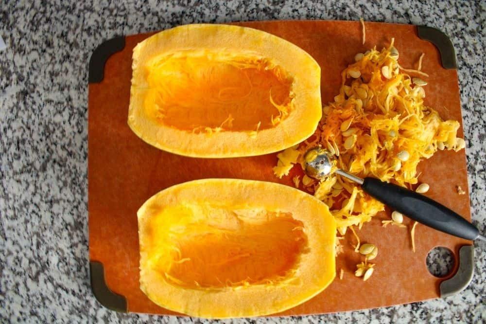 Spaghetti Squash cut in half on a cutting board with seeds cut out and melon baller to the side