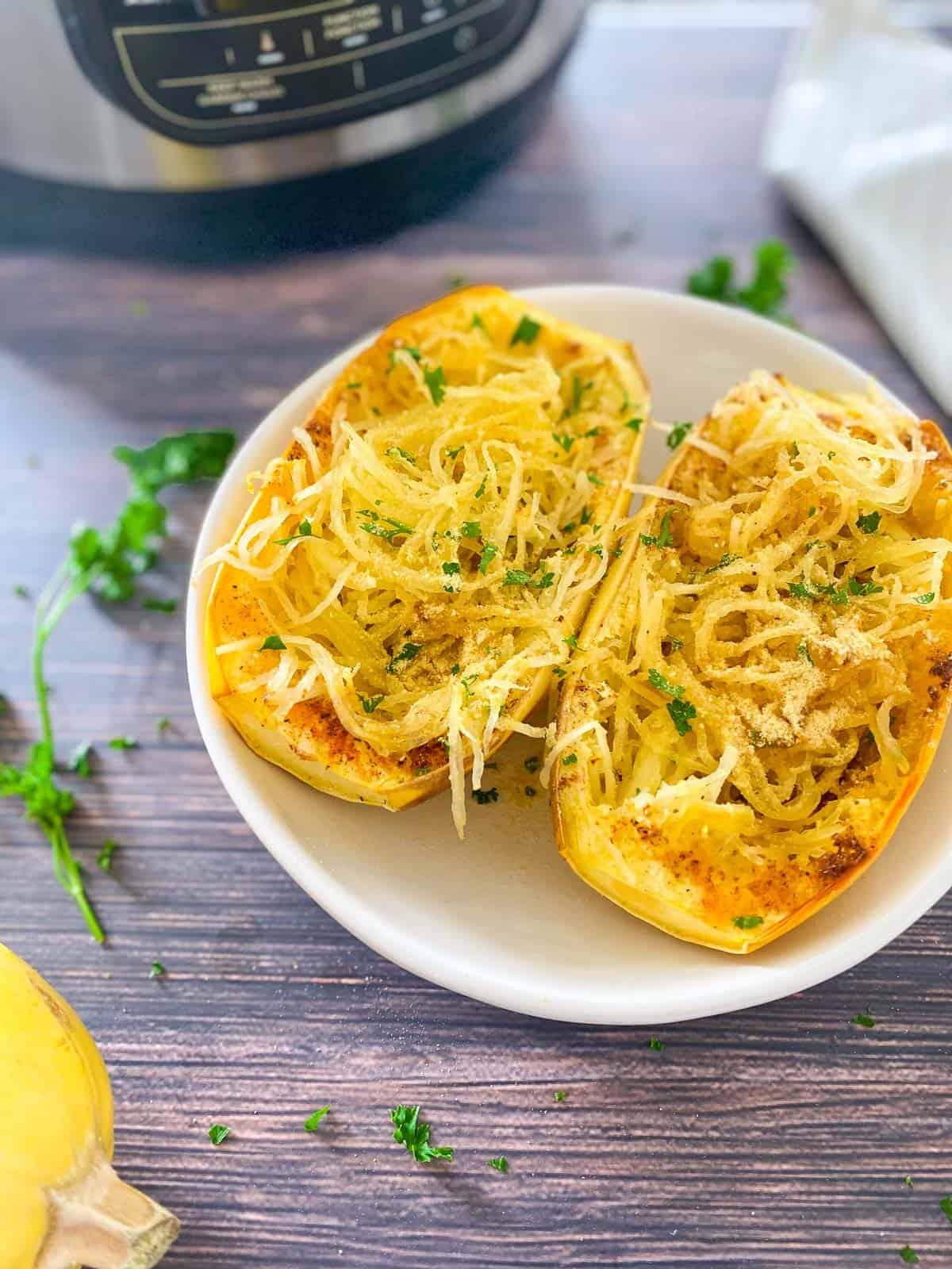 Two halves of a cooked spaghetti squash in a white dish with parsley garnish.