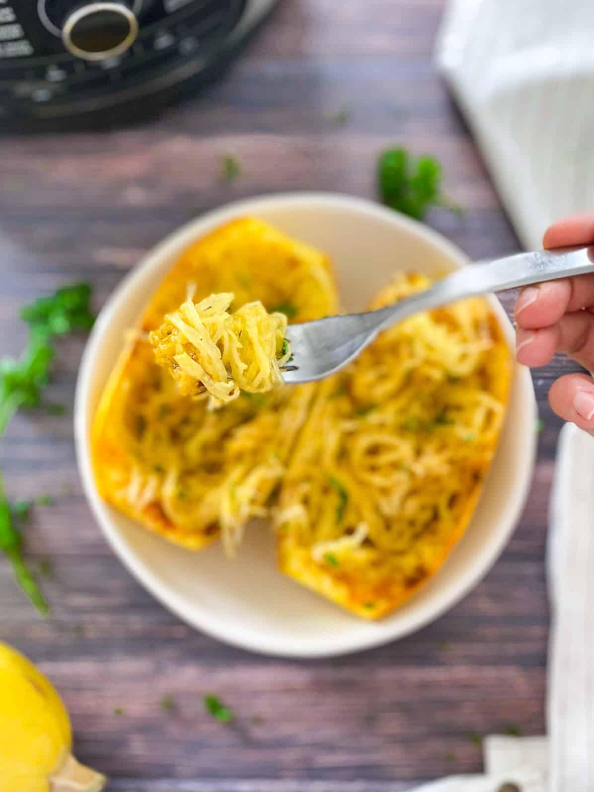 Fork full of spaghetti squash with halved spaghetti squash in a bowl below and air fryer in the background.