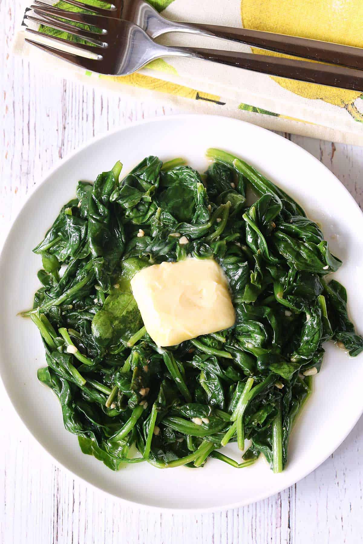 Sauteed spinach served on a white plate with a napkin and forks.