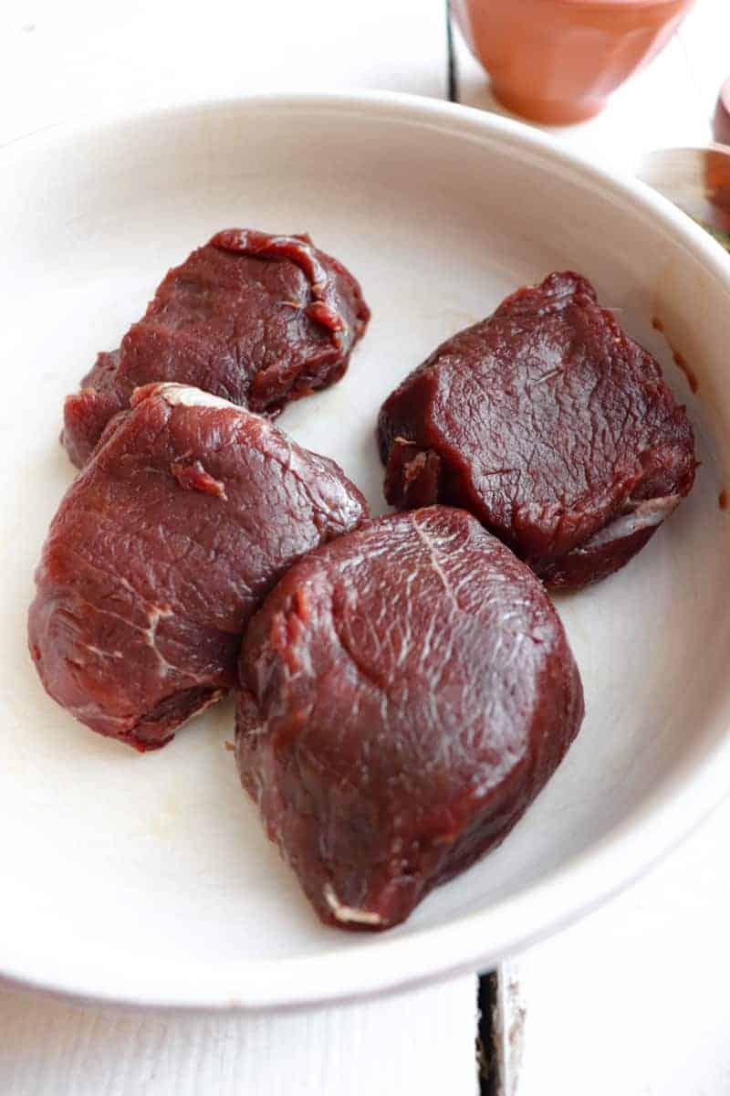 four raw venison medallions in a dish