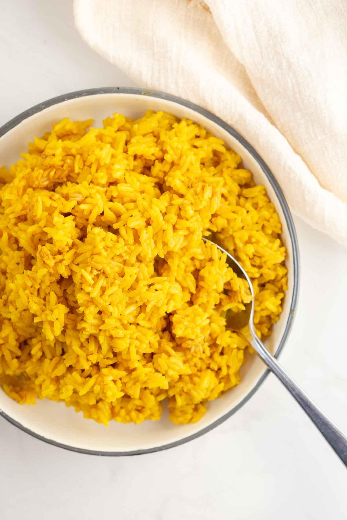 Plate of turmeric rice from above with spoon for serving