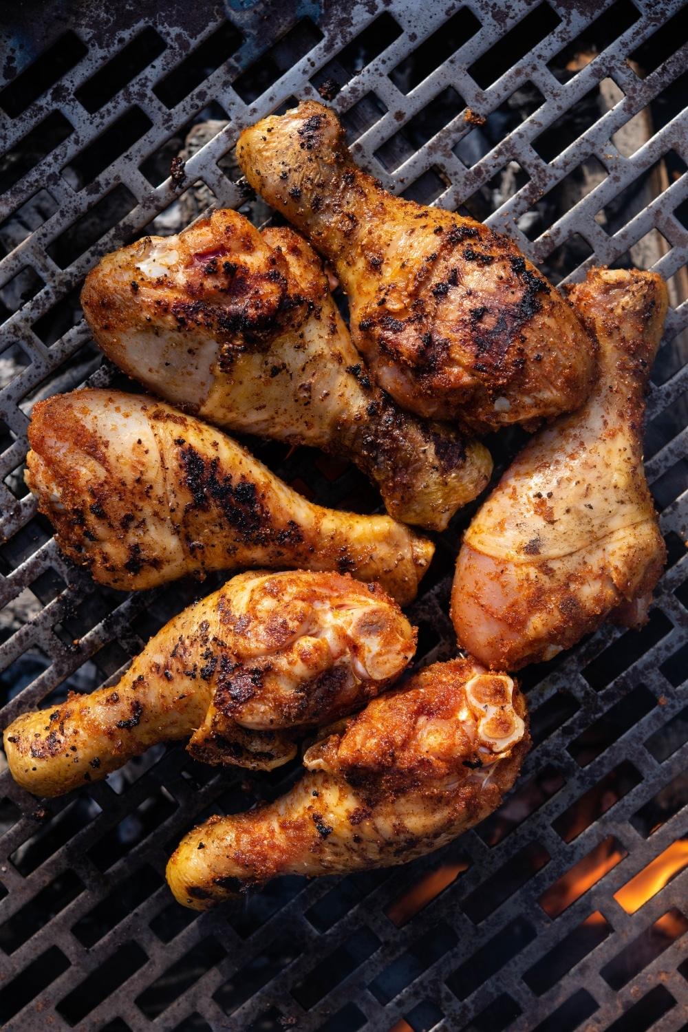 Seasoned chicken drumsticks cooking on a charcoal grill.