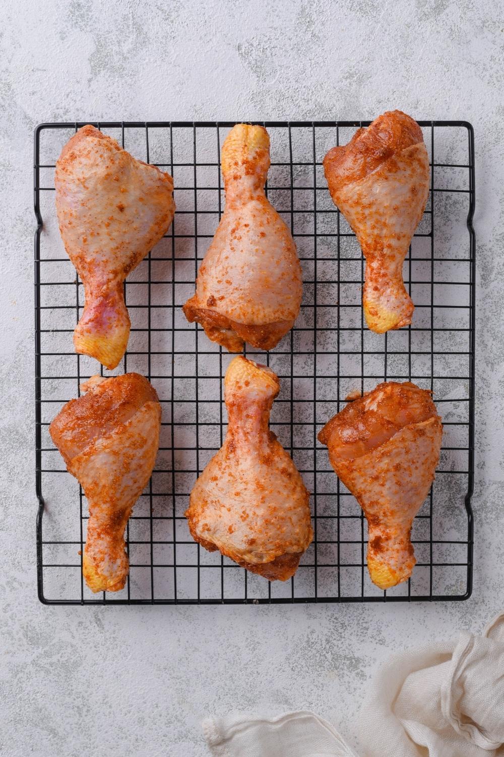 Six seasoned raw chicken drumsticks on a drying rack.