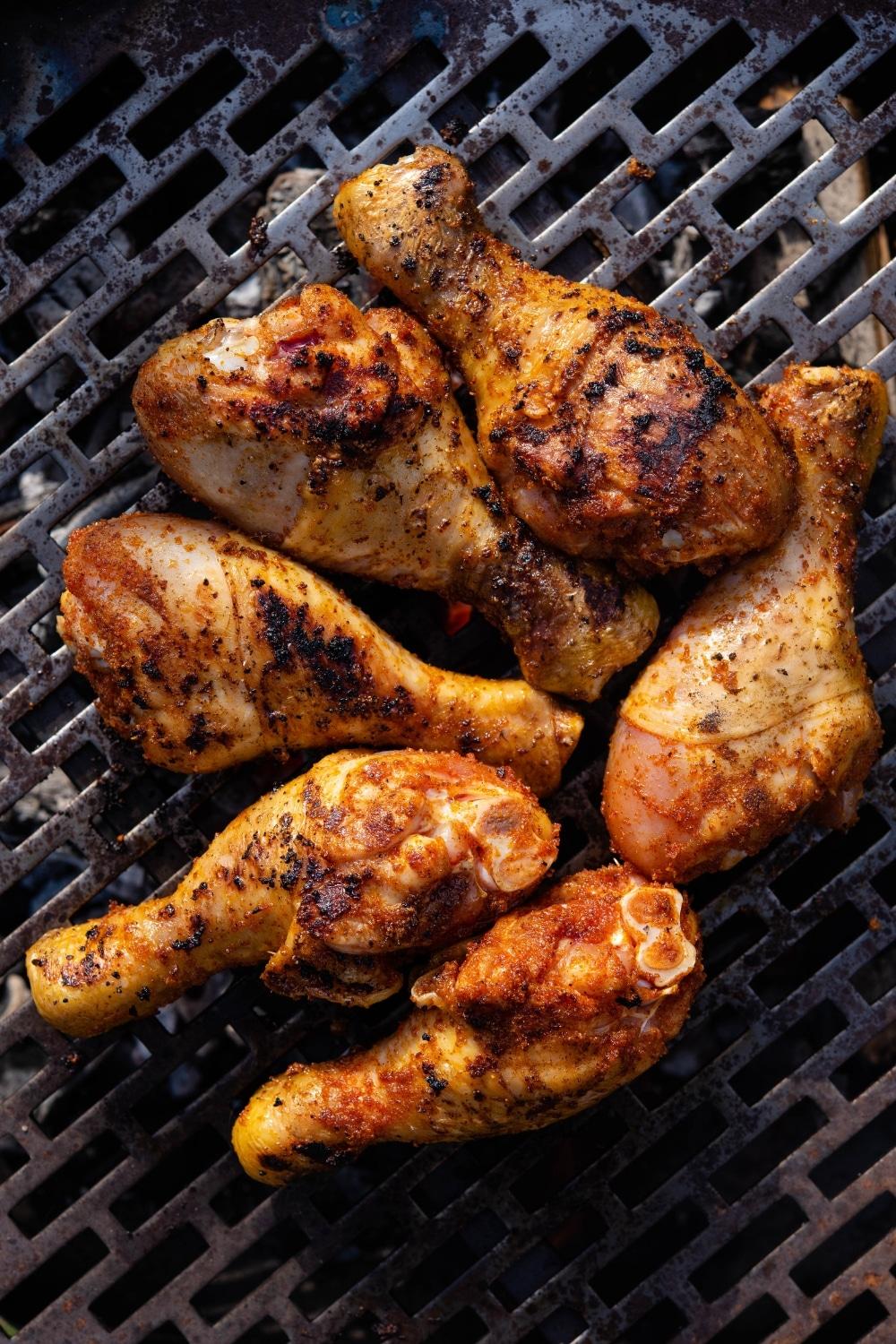 Six seasoned chicken drumsticks on a charcoal grill.