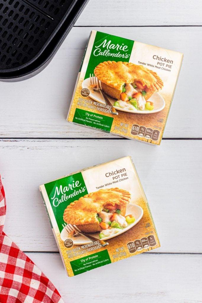 Two boxes of frozen pot pies on a white wooden table with an air fryer basket.