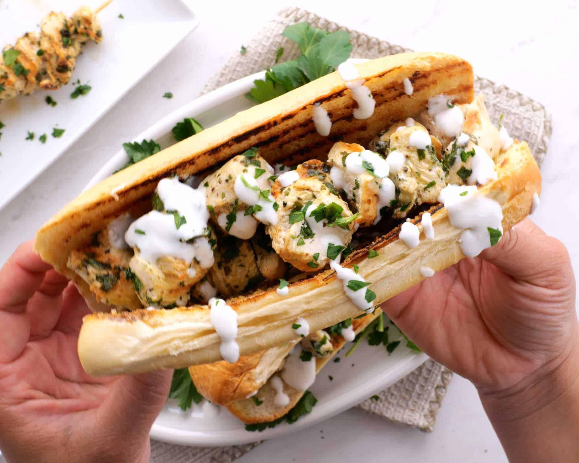 a hand holding a chicken spiedie drizzled with garlic sauce.