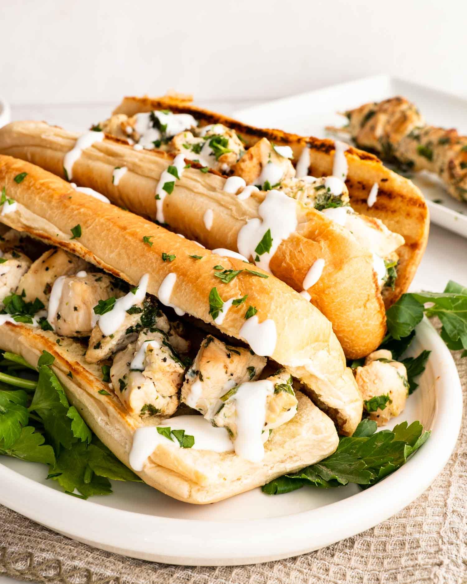 two chicken spiedies on a plate drizzled with garlic sauce.