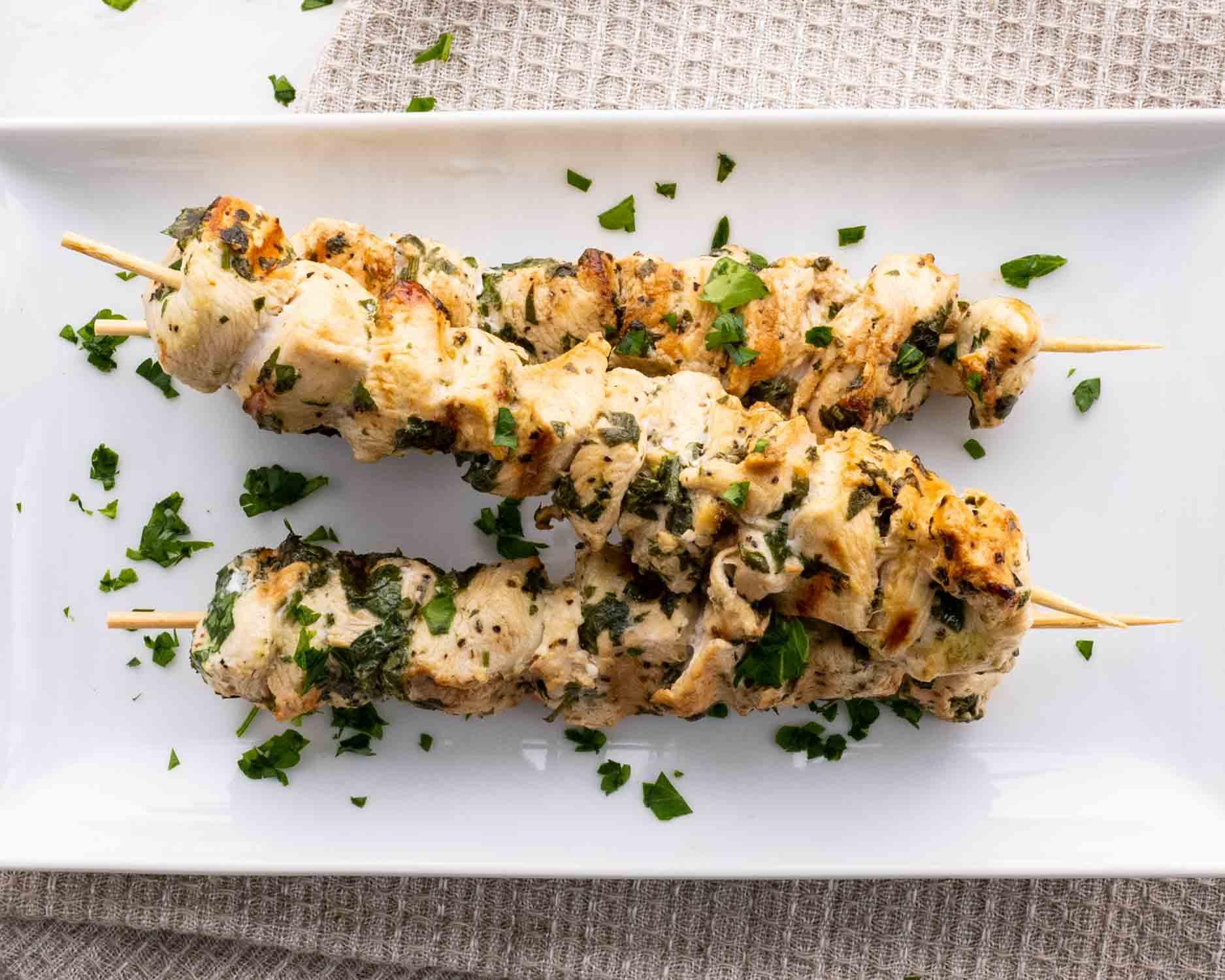 a few skewers of marinated chicken on a white platter.