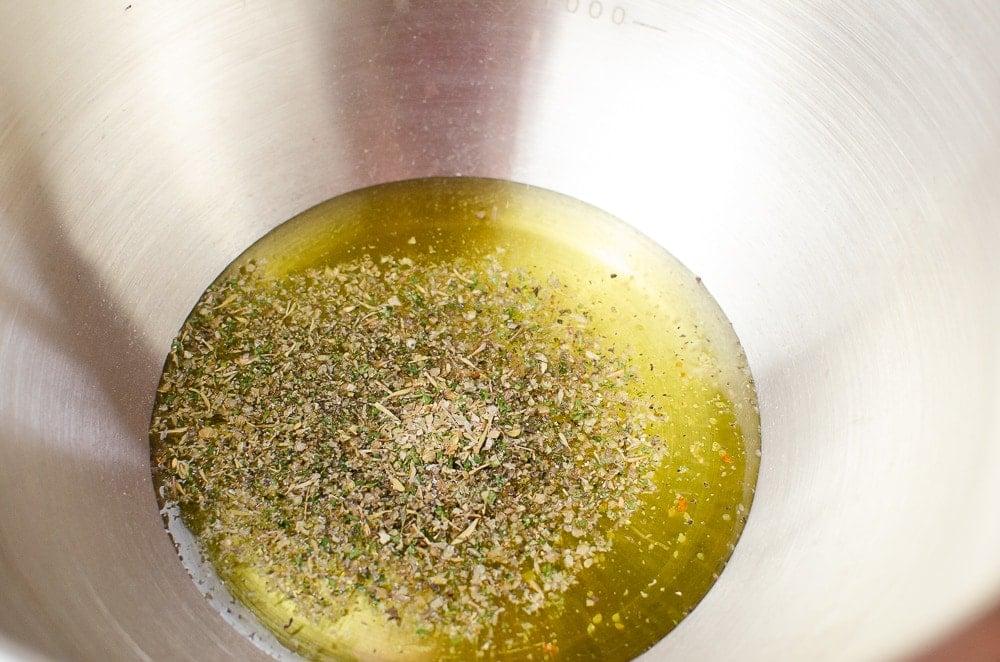 Olive oil and mixed herbs in a silver mixing bowl