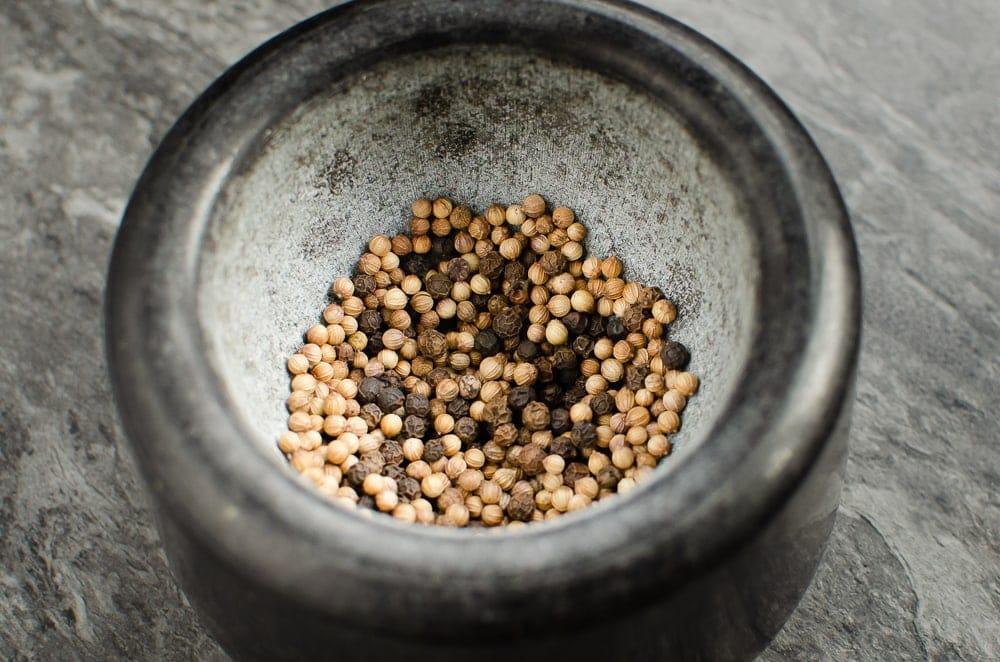 Peppercorns and coriander seeds in a black mortar ready to be crushed