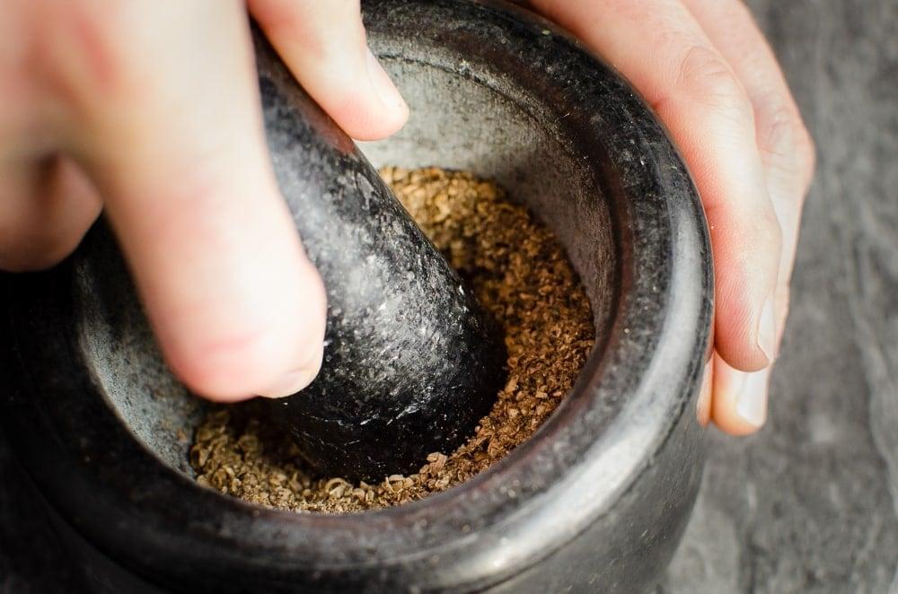 Crushing peppercorn and coriander seeds with a black pestle and mortar
