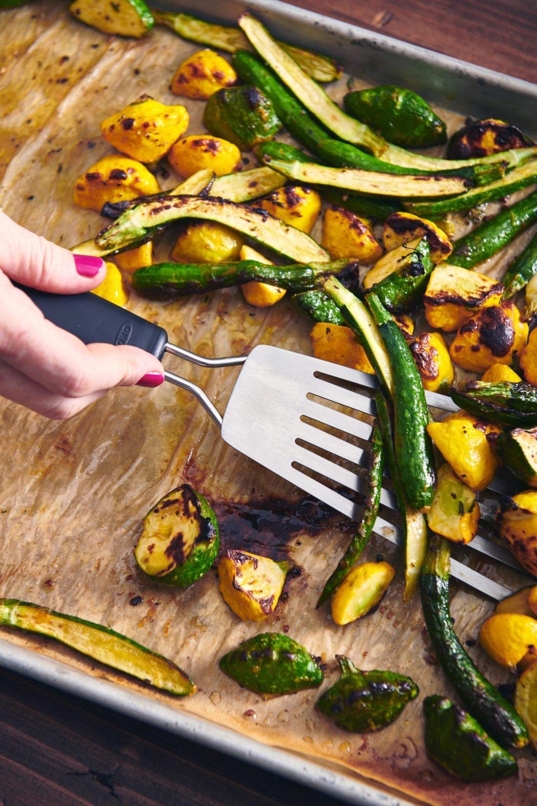 Woman using a spatula to grab Roasted Baby Squash from a lined baking sheet.