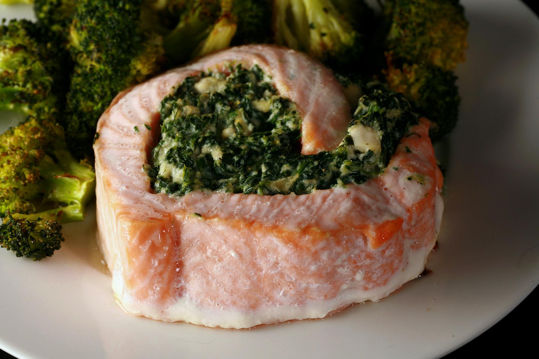 A serving of low carb spinach feta salmon pinwheels on a plate with some roasted broccoli.