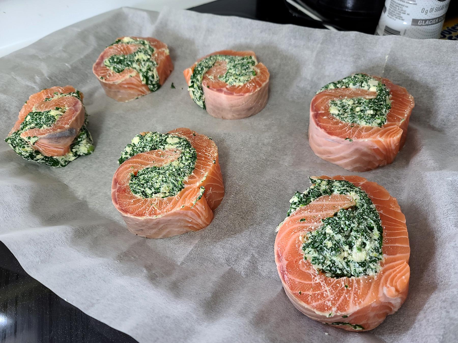 6 uncooked spinach feta salmon pinwheels on a parchment lined baking sheet.
