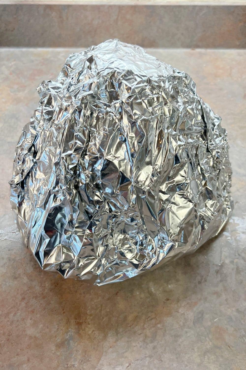 A spiral ham wrapped in foil in preparation to be cooked.