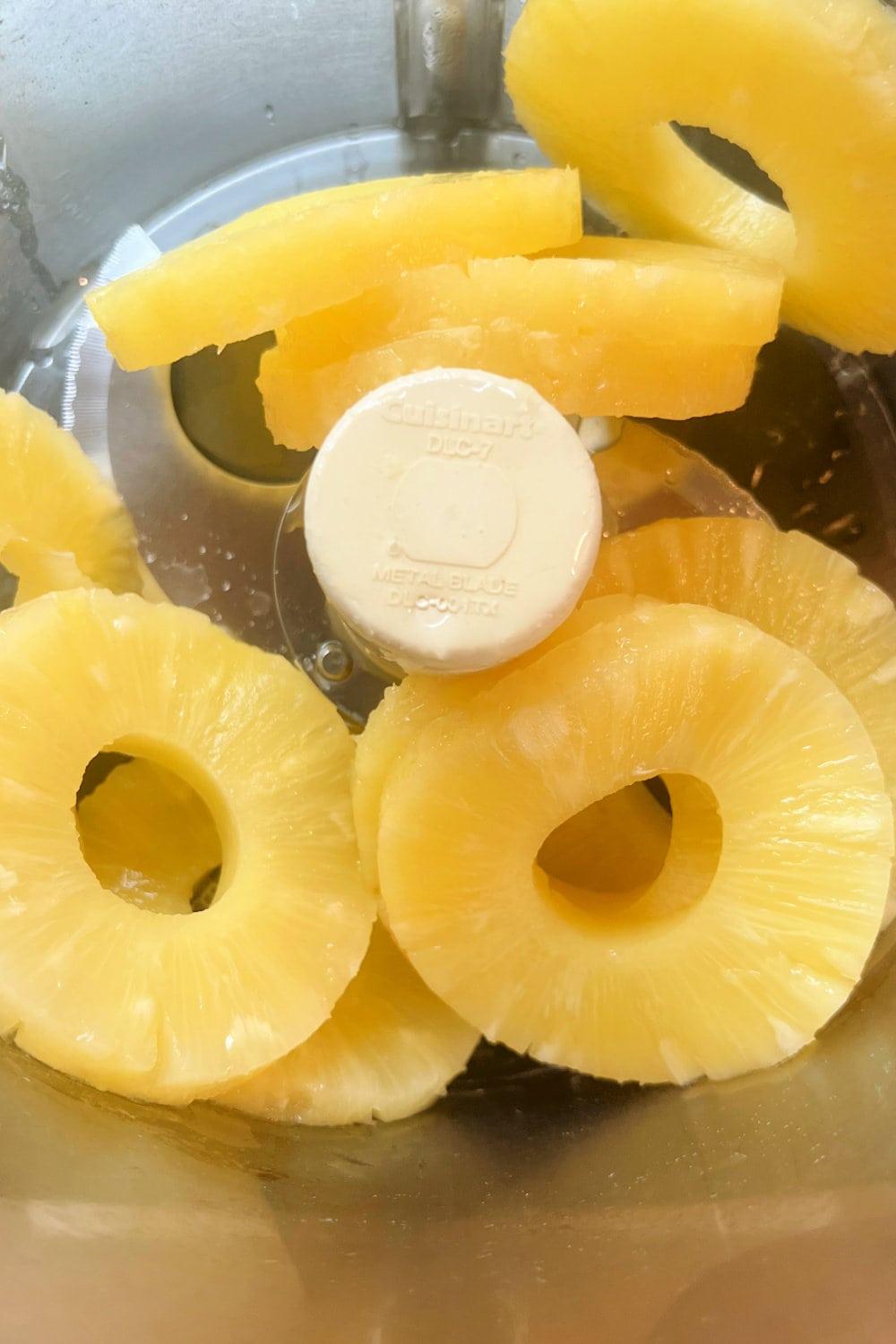 Canned pineapple rings in the bowl of a food processor.