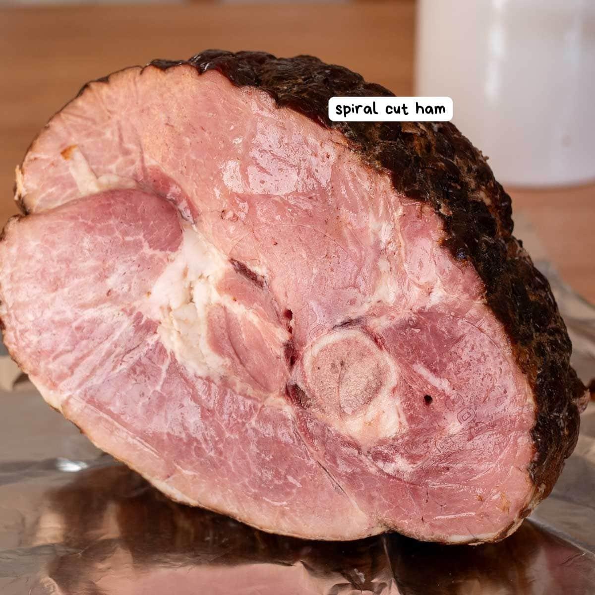 A close-up of a spiral cut ham with a brown crust and pink interior placed on a sheet of aluminum foil.