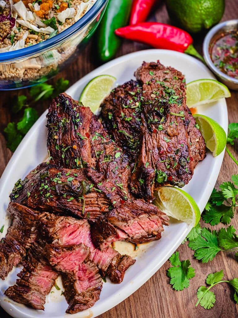 sliced beef flap meat on a platter with cilantro and limes