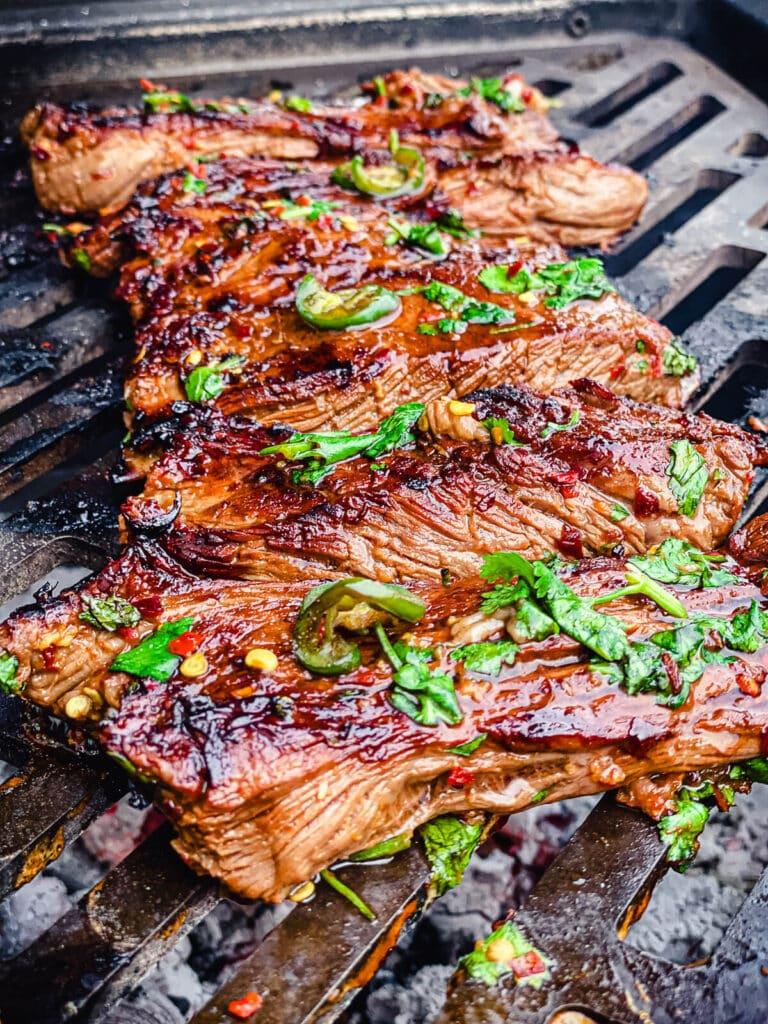 small flap steaks charring on a grill grate over hot coals