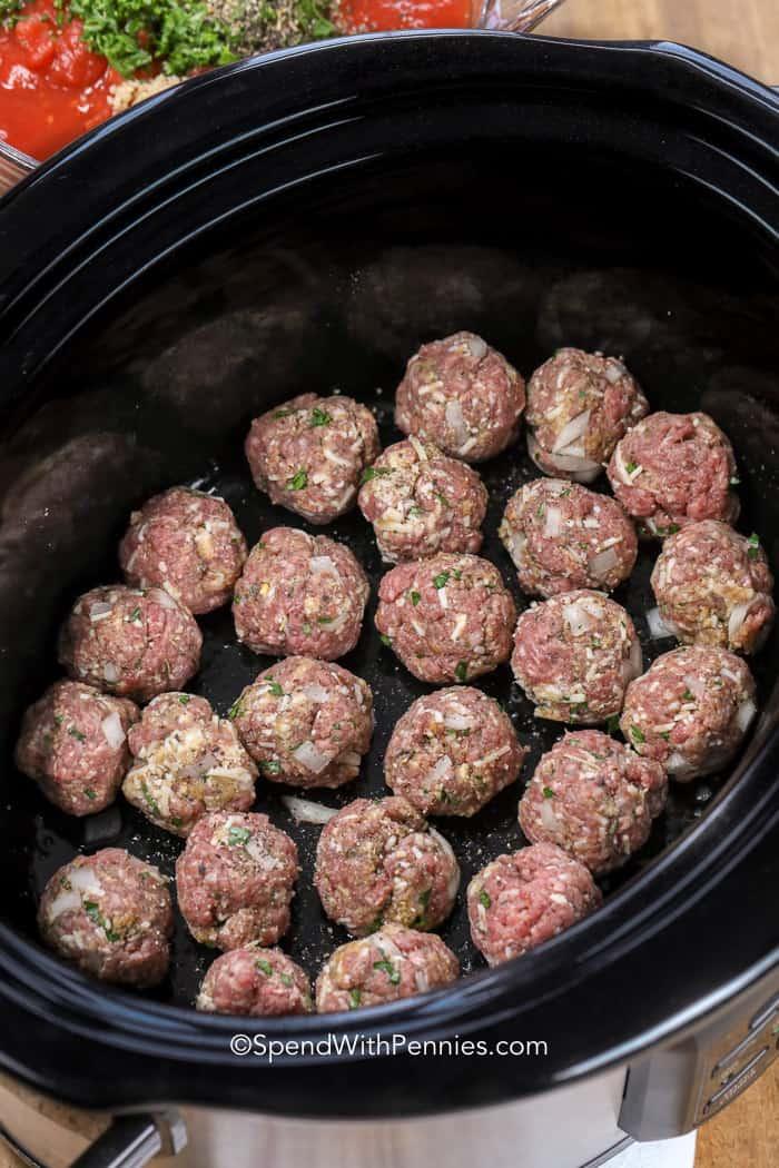 Uncooked meatballs in a black slow cooker