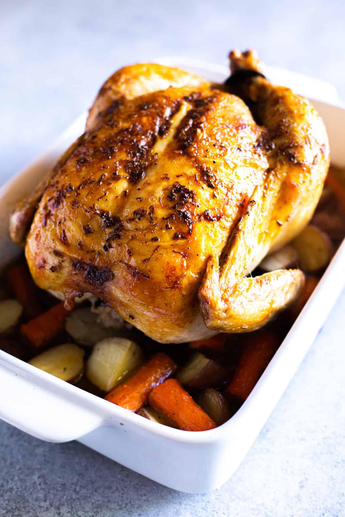 Roast Chicken on top of potatoes and carrots in a baking dish.