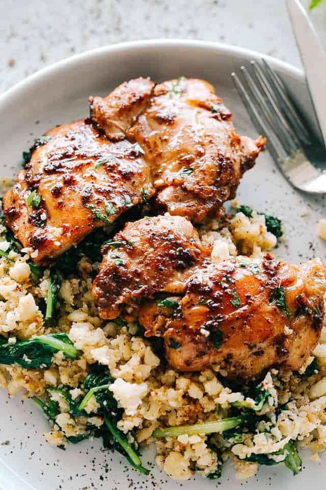 Cooked chicken thighs placed over a bed of cauliflower rice mixed with baby spinach.