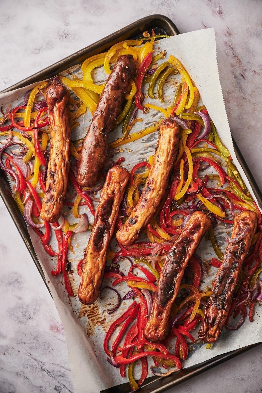 Roasted chicken sausages, bell peppers, and onions on a parchment paper lined baking tray.