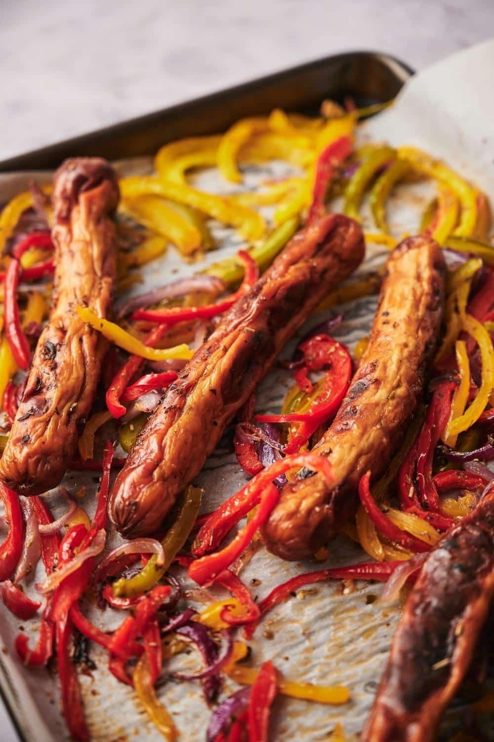 Roasted chicken sausages, peppers, and onions on a parchment paper lined tray set over a marble countertop.