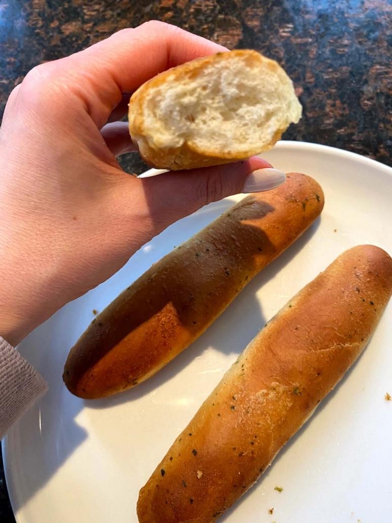 hand holding half of breadstick above plate with breadsticks