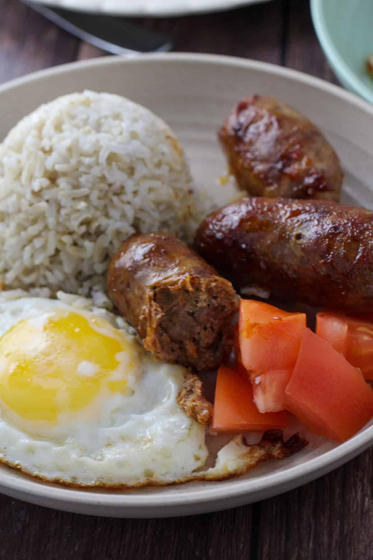 fried rice, fried egg, sliced tomatoes, and longganisa on a plate