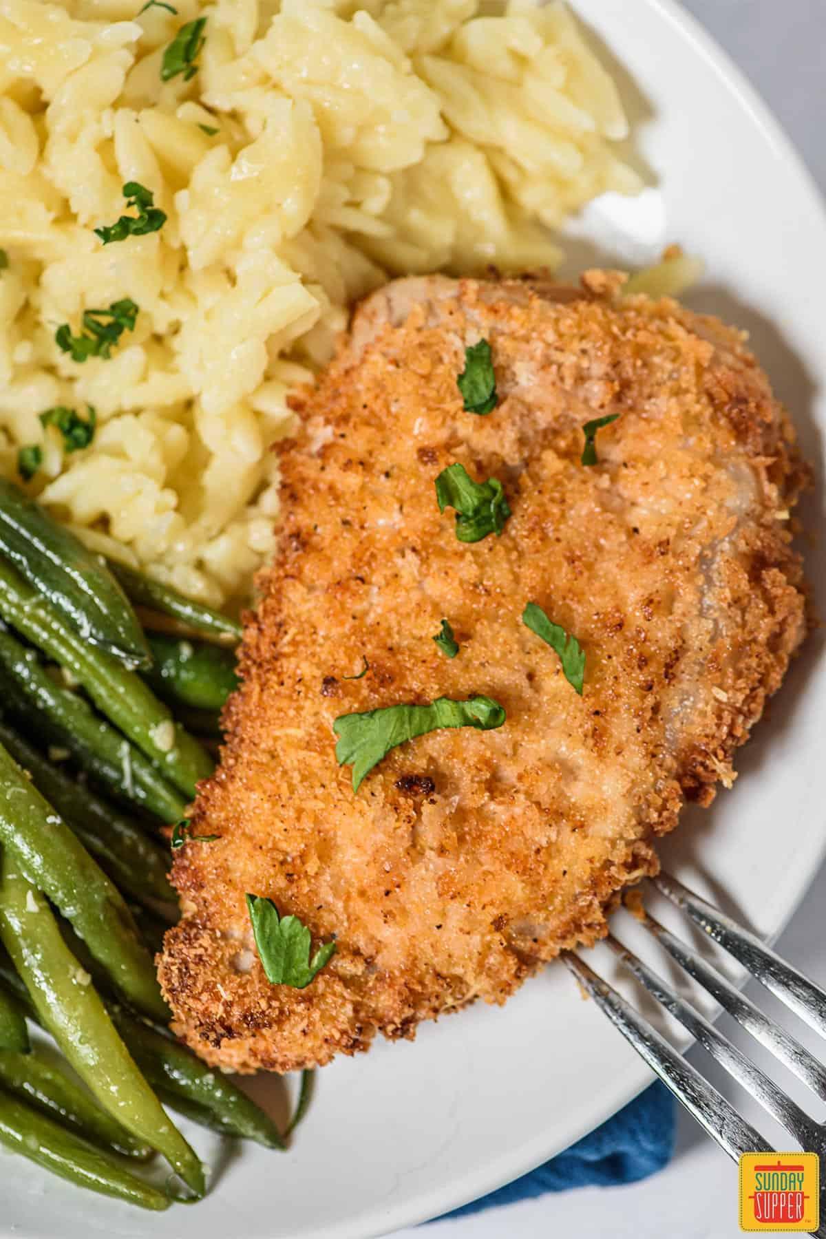 A plate with air fryer pork chops, orzo, and green beans