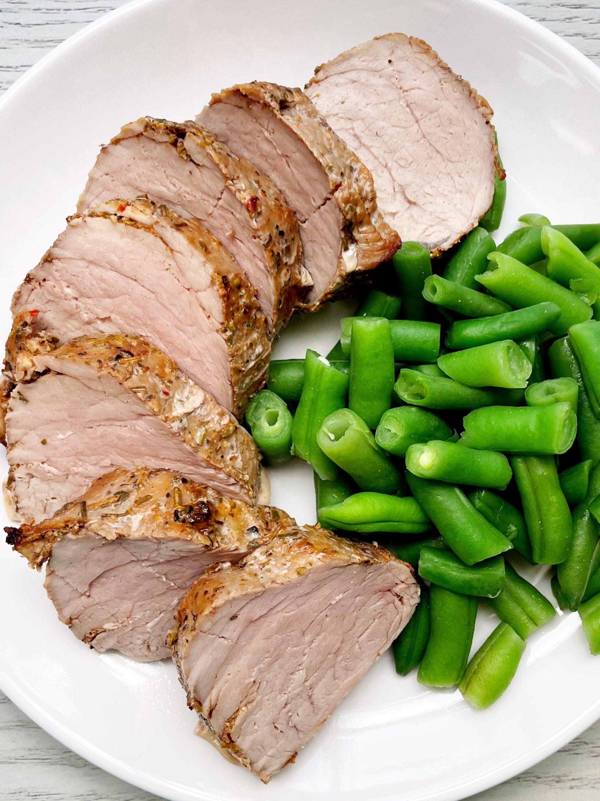 cooked pork tenderloin on a plate sliced with cooked green beans