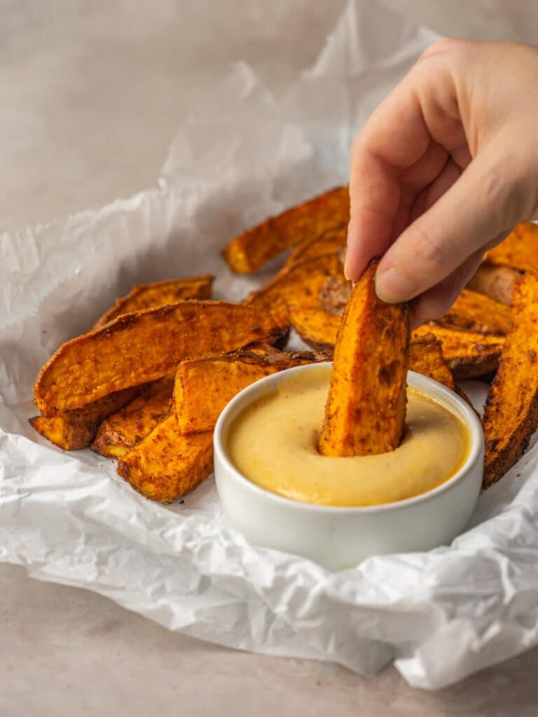 Side view of an air fryer sweet potato wedge dipping into garlic aioli