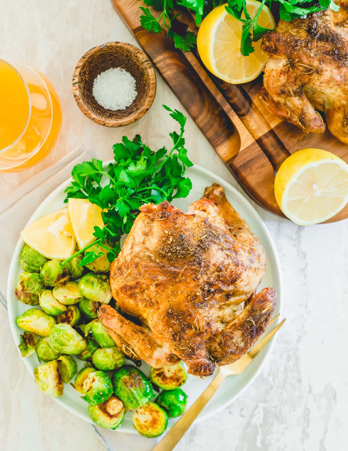 Tender juicy air fryer Cornish game hen cut into pieces on a plate with roasted Brussels sprouts.
