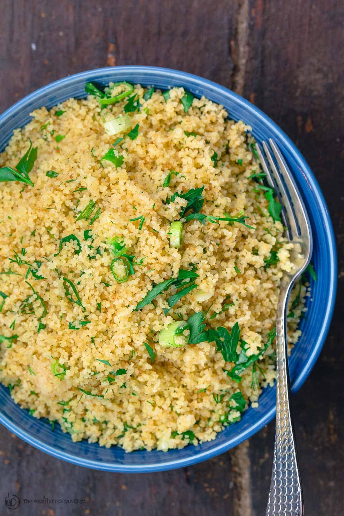 Cooked couscous in serving bowl, garnished with fresh herbs