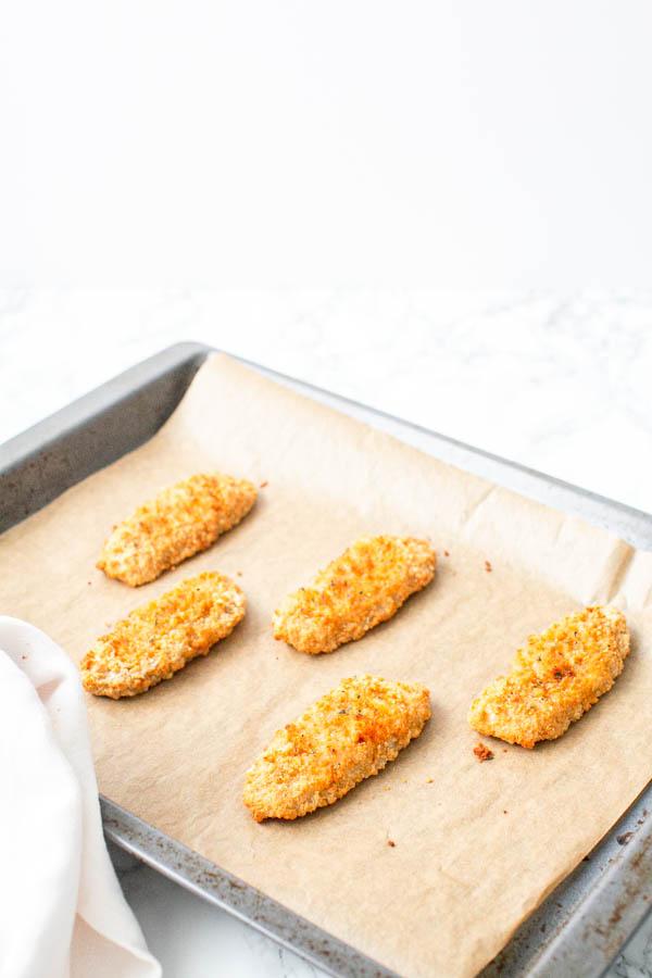Frozen breaded fish fillets in oven on a baking tray.