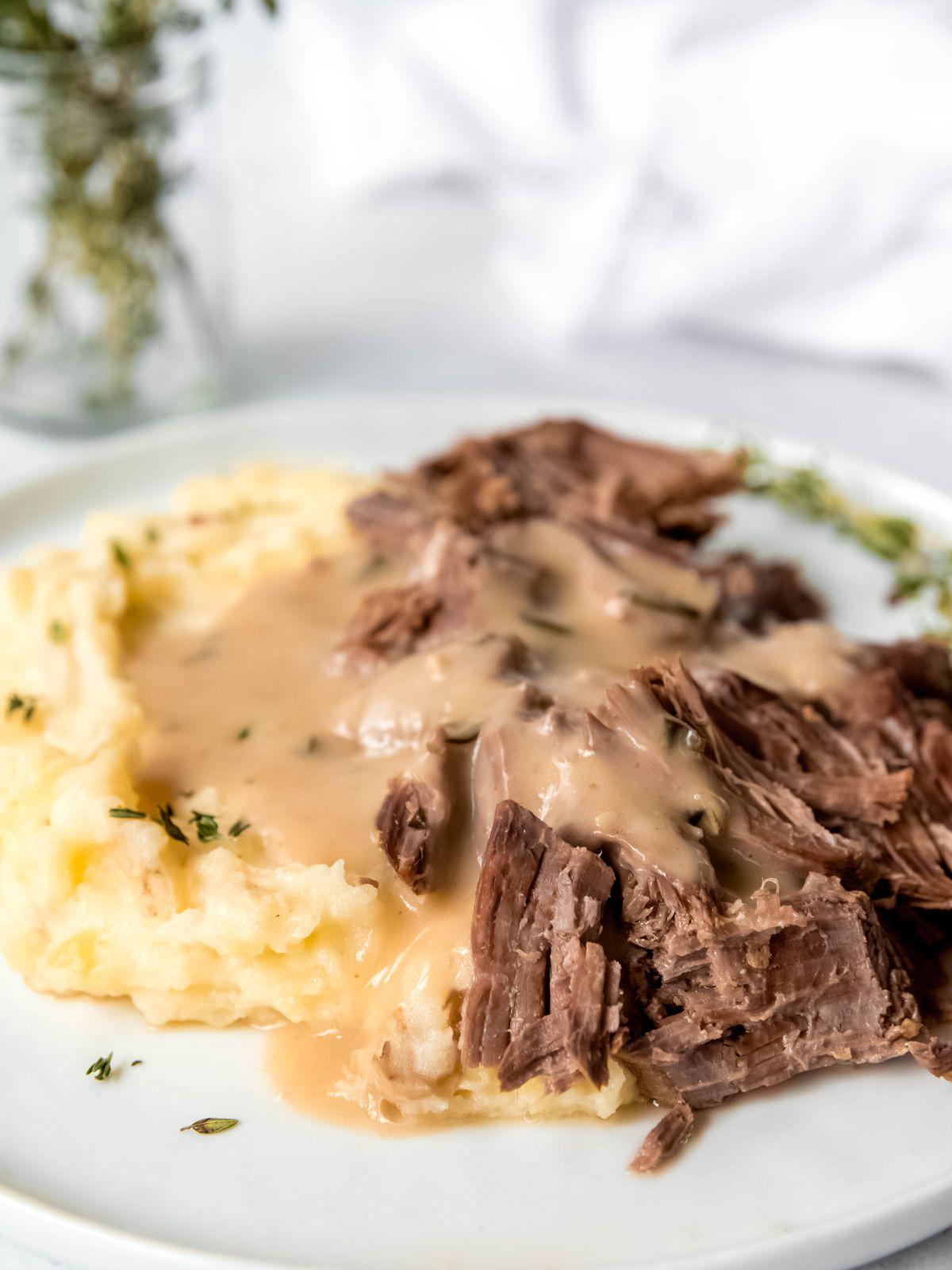 close up shot of shredded London broil beef roast with herbed brown gravy and mashed potatoes.
