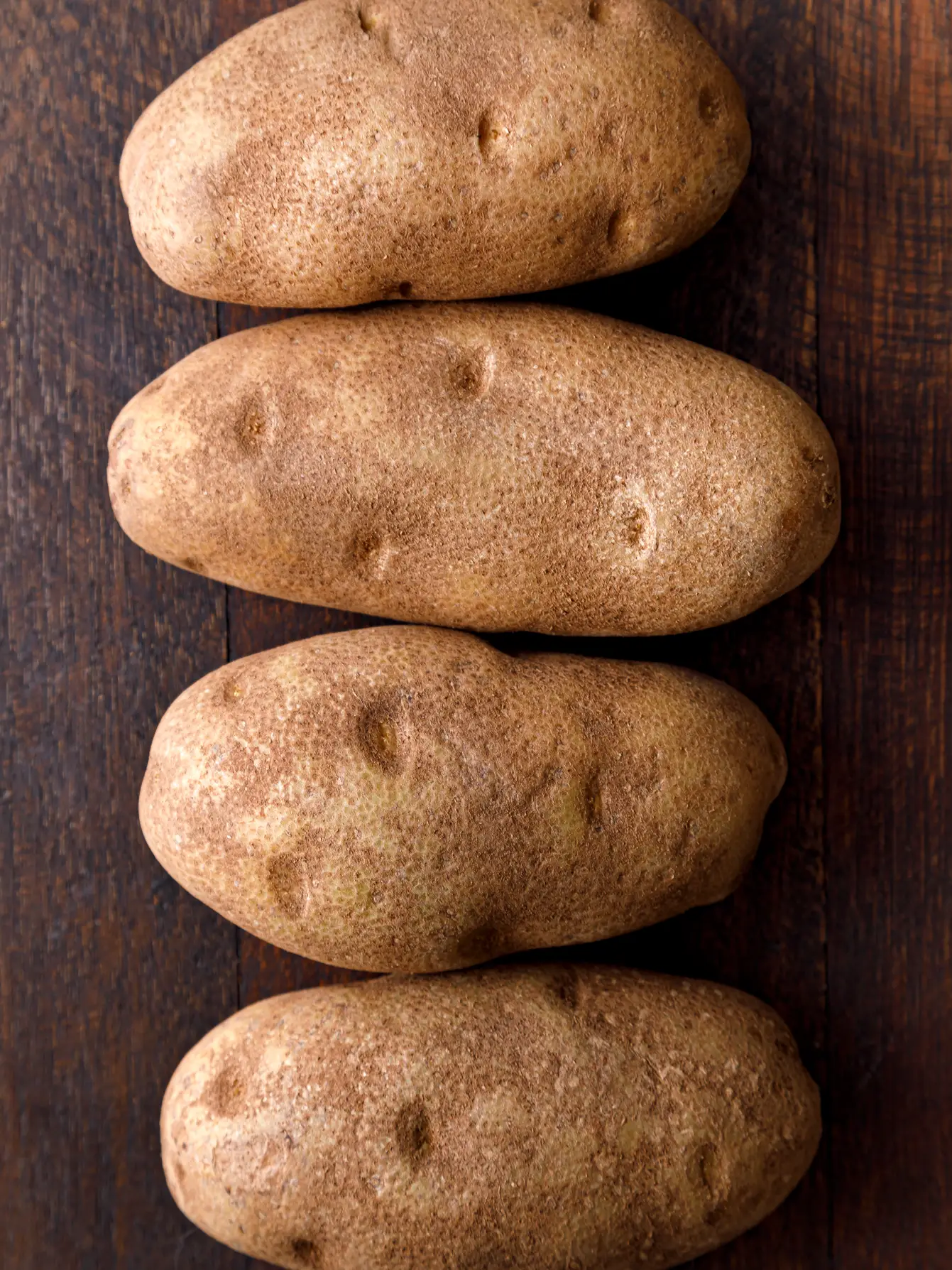 Four large russet potatoes lined up ready for baking