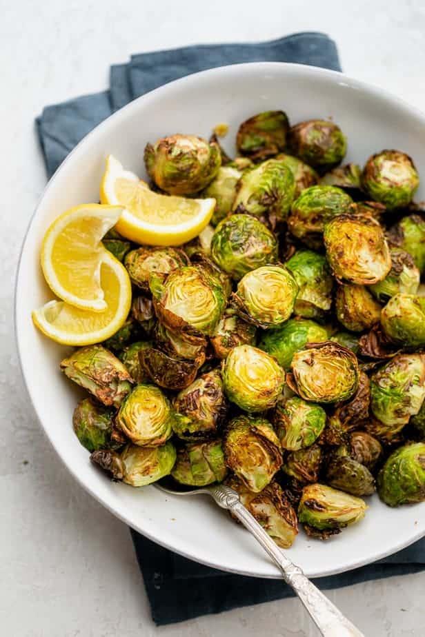 Air fryer brussel sprouts in a white bowl with lemon wedges