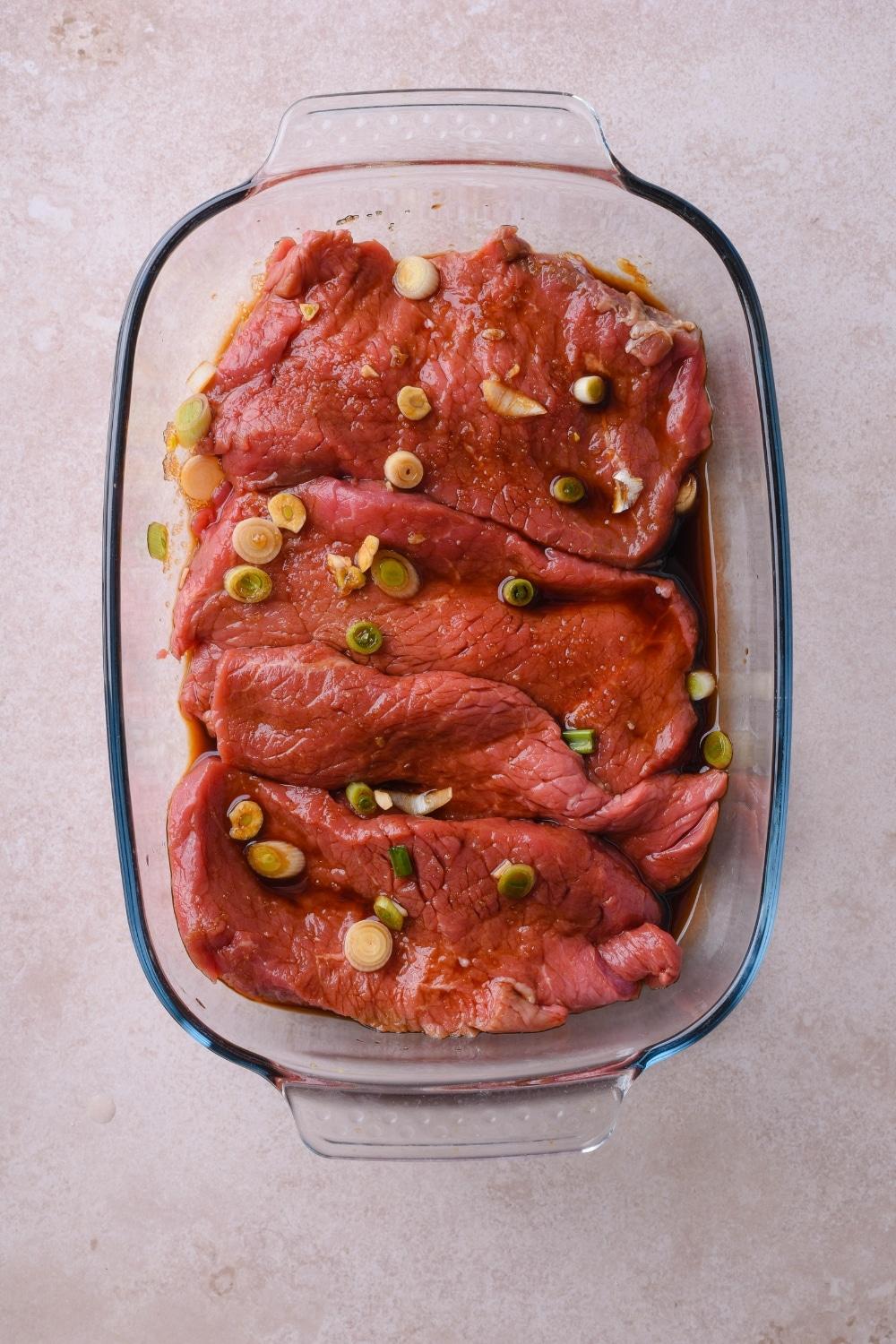Raw sirloin tip steak covered in marinade in a glass baking dish.