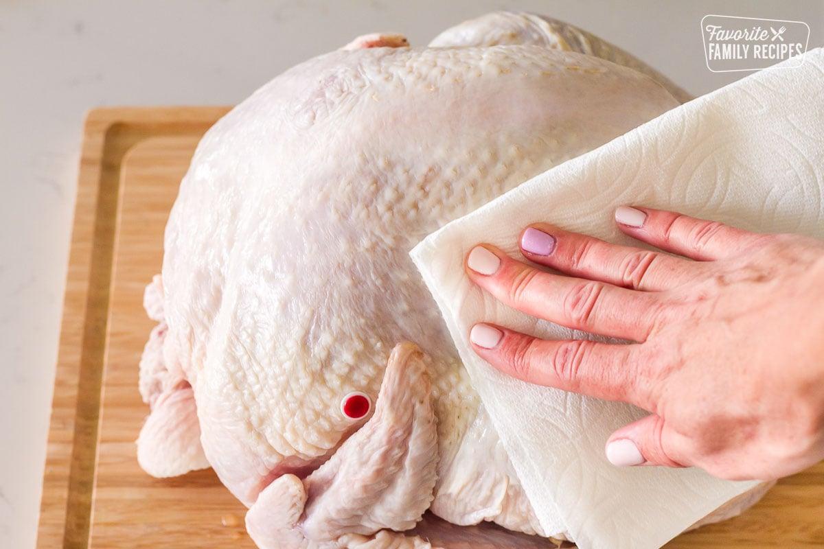 Hand patting turkey dry with paper towels